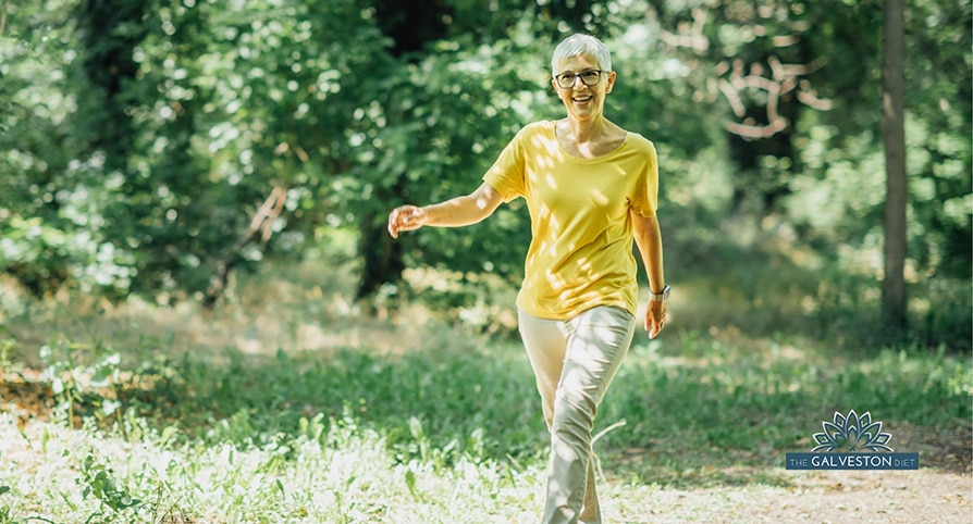 A middle aged woman in menopause smiles as she walks down a forested trail