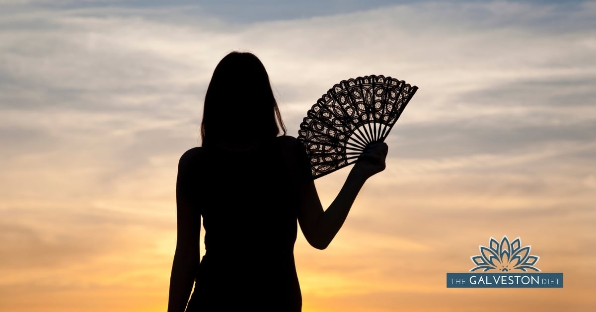 Silhouette of woman fanning herself watching a hot summer sunset.