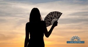 Silhouette of woman fanning herself watching a hot summer sunset.