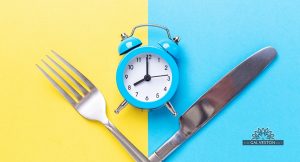 Blue and yellow background with a crossed knife and fork and a small blue clock to represent intermittent fasting